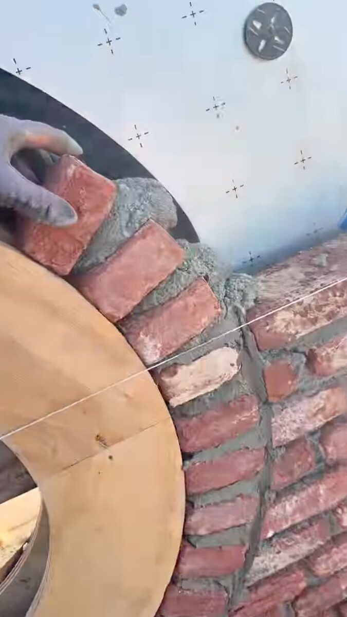Stenen van de rollaag rond het ronde venster worden één voor één tegen de houten mal gezet