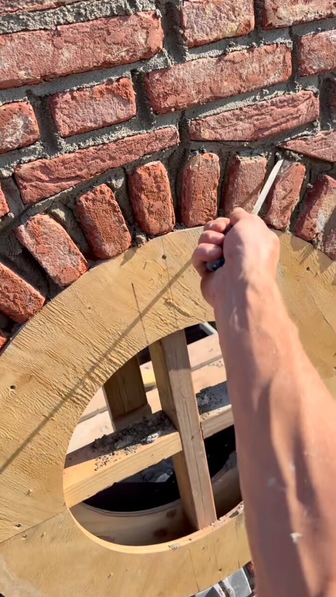 Een voegijzer haalt de voeg uit tussen de stenen van de rollaag boven het ronde venster