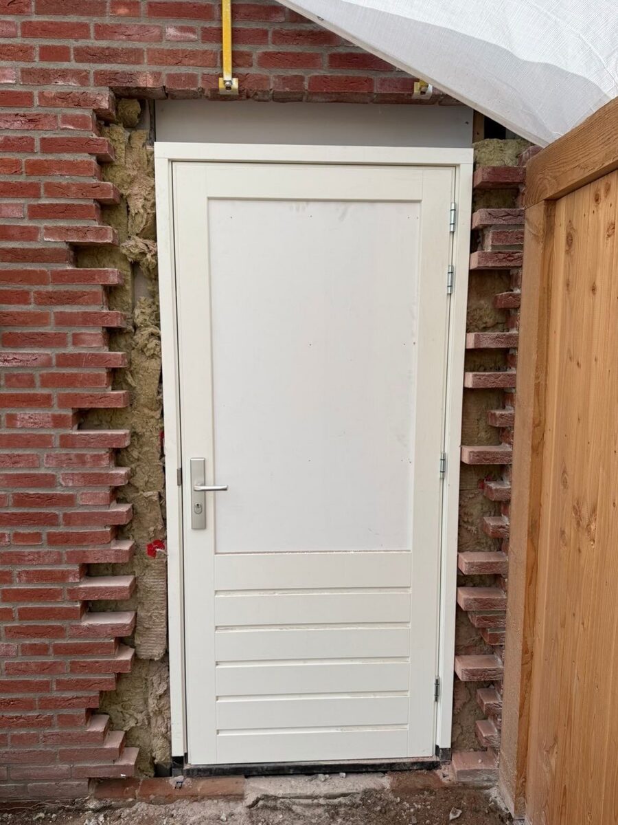 Voor: nieuwe deur in een bestaande bakstenen muur, de stenen rond het kozijn zijn nog open en gehavend