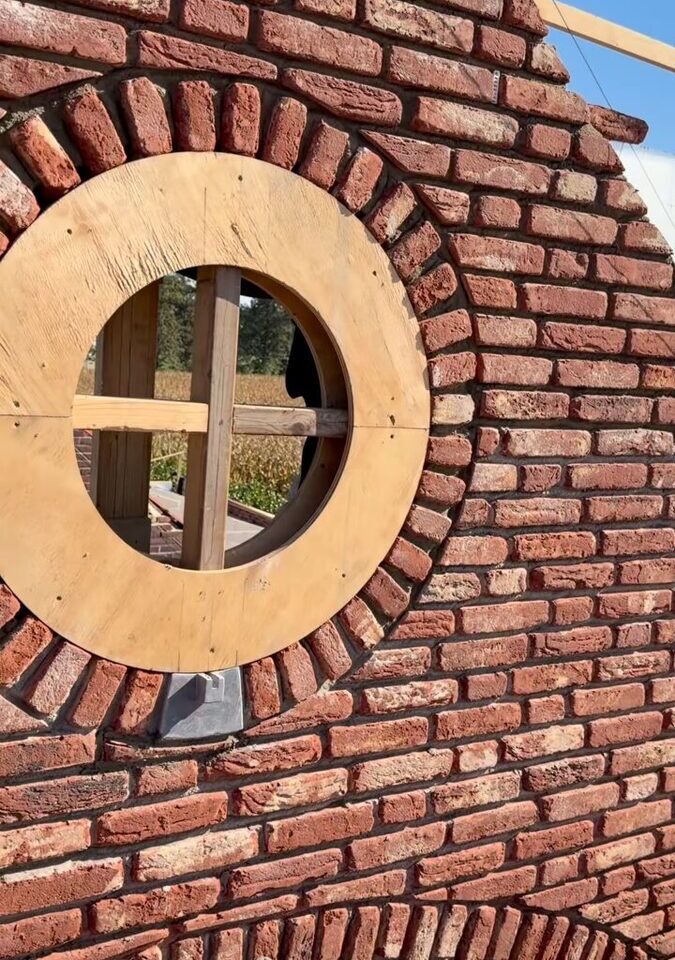 Rode bakstenen topgevel met een rond venster, de rollaag eromheen pas gemetseld, de mal nog in de opening