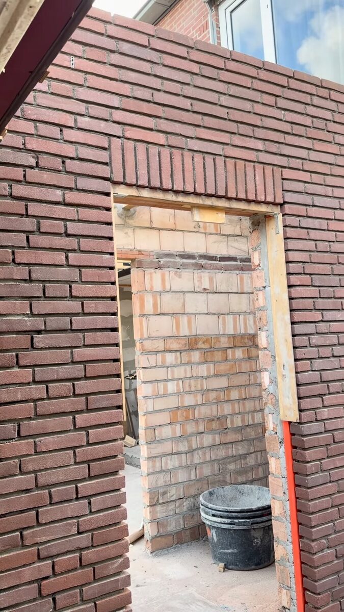 Nieuw gemetselde muur van rode steen met een doorgang en een rollaag erboven