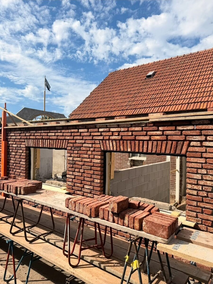 Woning met nieuw gemetselde gevel en segmentbogen boven de raamopeningen, op de steiger liggen stenen klaar